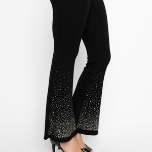 May include: Black flared pants with a sparkling rhinestone design at the hem. The pants are form-fitting and paired with black high-heeled platform sandals. The rhinestones create a gradient effect.