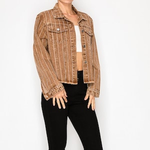 May include: A brown denim jacket with vertical white stripes, paired with black skinny jeans and black strappy heels. The jacket has a classic collar, button closures, and two chest pockets. The outfit is set against a white background.