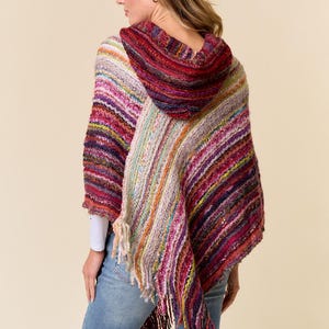 May include: A hooded poncho featuring a multi-colored striped knit pattern in shades of red, purple, orange, and cream. The garment has an asymmetrical hemline finished with long, dangling fringe tassels along the bottom edge.