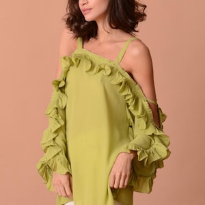 Könnte beinhalten: Ein limettengrünes Off-Shoulder-Top mit Rüschenärmeln und Trägern. Das Oberteil ist aus leichtem Stoff gefertigt und hat eine lockere, fließende Passform. Das Model trägt eine weiße Hose.