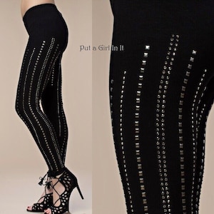 May include: Black leggings with vertical rows of silver studs and rhinestones. The leggings have a high waist and are form-fitting. The text "Put a Girl In It" is visible on the right side of the image. The model is wearing black high heels.