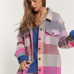 May include: A multi-colored plaid shirt jacket in shades of pink, gray, and beige. The jacket has two front pockets and button closures. The model is wearing a blue sweater underneath and a layered necklace.