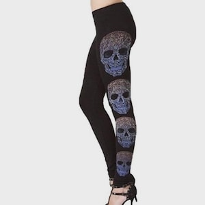 Könnte beinhalten: Schwarze Leggings mit einem sich wiederholenden Totenkopfmuster in Blau und Silber. Die Totenköpfe sind vertikal am linken Bein angeordnet. Die Leggings bestehen aus einem dehnbaren Stoff.