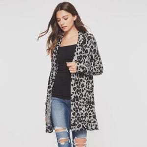 May include: A long, open-front cardigan in a gray and black leopard print. The cardigan is worn over a black top and blue jeans. The cardigan has two front pockets and long sleeves.
