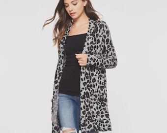 May include: A long, open-front cardigan in a gray and black leopard print. The cardigan is worn over a black top and blue jeans. The cardigan has two front pockets and long sleeves.