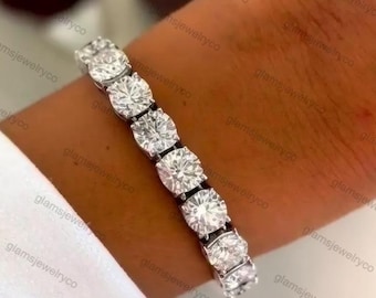 May include: A dazzling bracelet with a row of clear, round gemstones set in a silver or white metal. The gemstones are evenly spaced, reflecting light. The bracelet is displayed on a wrist, indicating it's a piece of jewellery.