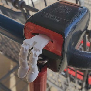 May include: A white, 3D-printed hand-shaped shopping cart coin holder. The holder is inserted into a black and red shopping cart handle. The handle has the text "25¢" and "Formatic" printed on it. The cart is blue and red.