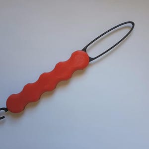 May include: A red and black tool with a wavy handle and a loop at the end. The handle is a bright red color, and the loop and the small hook are black. The tool is designed for a specific purpose.