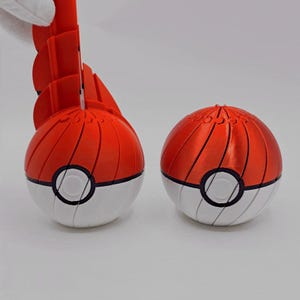 May include: Two red and white toy balls with black detailing. The top sections are red with vertical grooves, and the lower sections are white. Each ball features a black circle in the middle. One ball is partially open, showing a red interior.