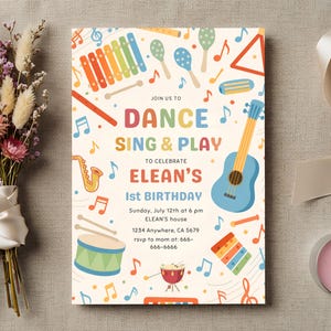 May include: A rectangular birthday invitation card with a cream background featuring colorful illustrations of musical instruments like a blue guitar, drum, saxophone, and xylophone, with the text JOIN US TO DANCE SING & PLAY TO CELEBRATE ELEAN'S 1st BIRTHDAY.