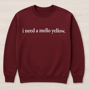 Puede incluir: Sudadera burdeos con la frase "i need a mello yellow." en blanco en el pecho. La sudadera tiene cuello redondo y mangas largas.