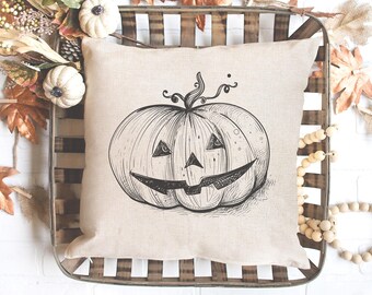 May include: A beige pillow with a black and white illustration of a jack-o'-lantern pumpkin. The pillow is in a wooden crate with fall-themed decorations.