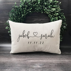 May include: A white pillow with the names "jacob" and "sarah" written in black cursive script with a heart symbol between the names. The date "11.11.22" is written below the names.