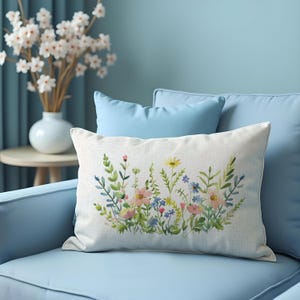 May include: A white throw pillow with a floral design featuring pink, yellow, and blue flowers on a green stem. The pillow is sitting on a light blue couch.