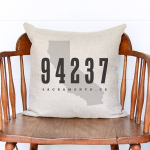 May include: A beige linen pillow with a black outline of the state of California and the text "94237 Sacramento, CA".