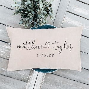 May include: A beige throw pillow with the text "matthew &hearts; taylor" and the date "4.15.22" printed in black.