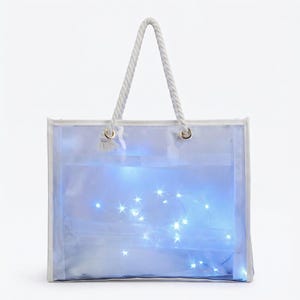 Może przedstawiać: Przezroczysta torba typu tote z białym wykończeniem i sznurkowymi uchwytami. Torba jest podświetlona małymi, migoczącymi białymi światełkami, tworzącymi delikatną poświatę. Torba jest przeznaczona do przenoszenia przedmiotów.