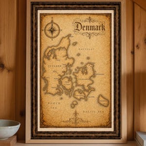 Op de afbeelding: Een ingelijste vintage kaart van Denemarken met een kompasroos en de naam van het land in een elegant lettertype. De kaart is in bruin- en beigetinten, met de tekst "Denmark" bovenaan. De lijst is donkerbruin.