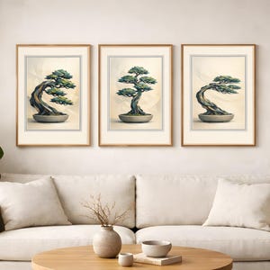 Op de afbeelding: Drie ingelijste prenten van bonsai-bomen. Elke prent toont een andere bonsai-boom in een grijze pot tegen een crèmekleurige achtergrond. De lijsten zijn lichtbruin. De prenten worden boven een crèmekleurige bank weergegeven.