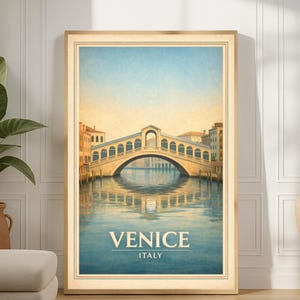 Puede incluir: Una impresión enmarcada que presenta el Puente de Rialto en Venecia, Italia. La obra de arte representa el puente sobre un canal con edificios a ambos lados, bajo un cielo azul. Las palabras "VENICE" e "ITALY" están impresas en la parte inferior.