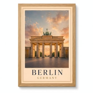 Op de afbeelding: Een ingelijste kunstdruk met de Brandenburger Tor in Berlijn, Duitsland, bij zonsondergang. De afbeelding toont het neoklassieke monument met het quadriga-beeldhouwwerk onder een oranje lucht. De tekst BERLIN GERMANY staat onder de afbeelding.