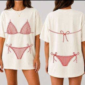 May include: An off-white short-sleeve t-shirt featuring a red line-art graphic of a bikini. The front displays the bikini top and bottom, while the back shows the bikini bottom and the tied strings of the top, all rendered in a simple red outline.