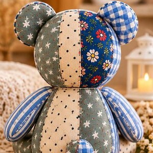May include: A patchwork teddy bear constructed from various fabric patterns including blue and white gingham, sage green with white stars, cream with black polka dots, and a dark blue floral print with red and white daisies, featuring round ears.
