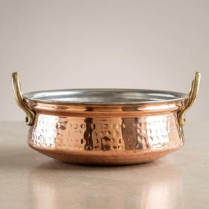 May include: A copper-colored bowl with a hammered texture and two brass handles. The interior of the bowl is silver. This decorative bowl is ideal for serving food.