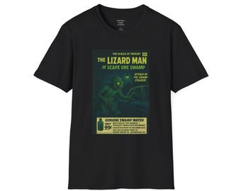 May include: Black t-shirt featuring a vintage-style graphic. The graphic includes the text "THE LIZARD MAN OF SCAPE ORE SWAMP" with an illustration of a swamp creature. The shirt also has the text "GENUINE SWAMP WATER".