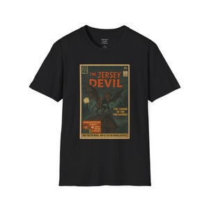 Peut inclure: T-shirt noir avec un design de couverture de bande dessinée vintage. Le graphisme affiche "The Jersey Devil" avec une illustration de créature menaçante. Le texte supplémentaire comprend "The Terror of the Pine Barrens".