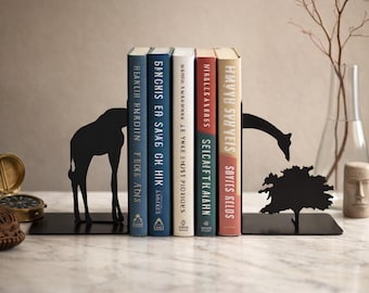 May include: Black metal giraffe bookends holding a row of colorful books. The bookends feature a giraffe silhouette on each end, with a tree silhouette on one. The books have titles in a foreign language.