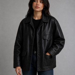 May include: A black leather jacket with a classic design. The jacket features a collared neckline, button-down closure, two chest pockets, and two side pockets. The model is wearing a black shirt and blue jeans.