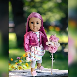 May include: A doll with long purple hair, wearing a pink jacket, a white dress with colorful stars, gray leggings, and pink shoes. The doll is holding a pink unicorn stick toy. The background is a blurred outdoor scene.