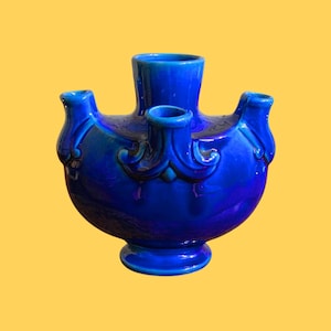 Pode incluir: Um vaso de cerâmica azul cobalto com um design único. O vaso tem um corpo redondo com três bicos e uma abertura central. Enfeites decorativos adornam o corpo. O vaso tem aproximadamente 18 cm de altura.