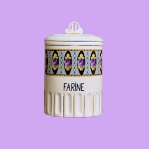 Könnte beinhalten: Ein cremefarbener Keramikbehälter mit Deckel, mit einem dekorativen Band aus lila floralen Designs und dem Wort "FARINE" in Schwarz. Der Behälter hat vertikale Rillen und einen goldenen Rand.