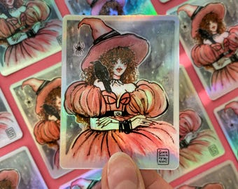 May include: A holographic sticker featuring a witch with long brown hair wearing a pink dress and a pointed hat. She is holding a black raven in her left hand. The background is a sparkly, light blue with white stars. The sticker has the text "Gina Silva 2022" in the bottom right corner.