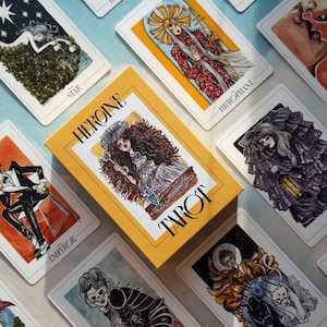 May include: A tarot deck with a yellow box featuring the text "Heroine Tarot". The cards feature illustrations of people and symbols in a dark, whimsical style.
