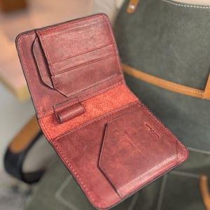 Pode incluir: Carteira de couro bordô aberta, com várias ranhuras para cartões e um compartimento para notas. A carteira tem uma superfície texturizada e uma borda escura. O interior é de um tom bordô mais claro.