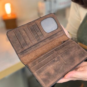 Op de afbeelding: Open bruin leren portemonnee met meerdere kaartsleuven en een doorzichtig ID-venster. De portemonnee heeft een distressed afwerking, met kleur- en textuurvariaties. De binnenkant is gevoerd met een lichter bruin materiaal.