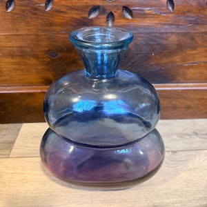 May include: A two-part, blue glass vase with a rounded bottom and a smaller, rounded top. The vase has a flared opening and a gradient color that transitions from blue to purple.