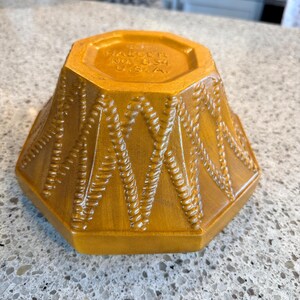 May include: A golden-yellow, octagonal ceramic bowl with a textured, woven pattern. The bowl's base features the text "HAUSER NO. 834 U.S.A."
