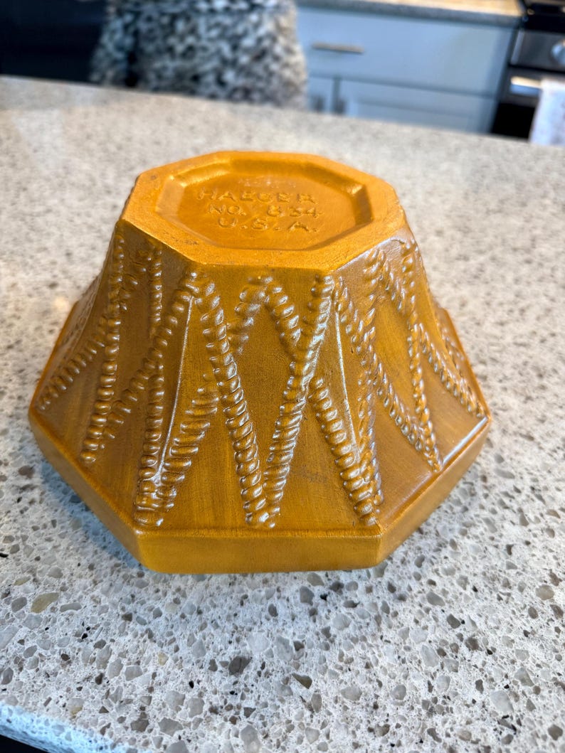 May include: A golden-yellow, octagonal ceramic bowl with a textured, woven pattern. The bowl's base features the text "HAUSER NO. 834 U.S.A."