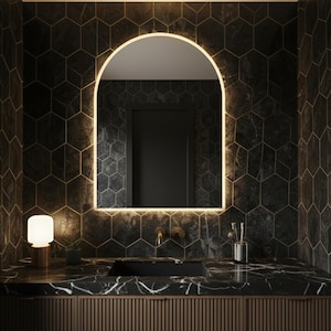 以下が含まれることがあります： 黒い大理石のカウンタートップと木製の洗面化粧台を備えたモダンなバスルーム。光るフレームのアーチ型ミラーがシンクの上にあります。壁は暗い六角形のタイルで覆われ、カウンターには小さなランプが置かれています。