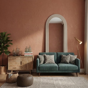 May include: A teal two-seater sofa with patterned throw pillows sits in front of a large arched mirror. A wooden cabinet with glass bottles and a floor lamp are also in the room. The wall is painted a warm terracotta color.