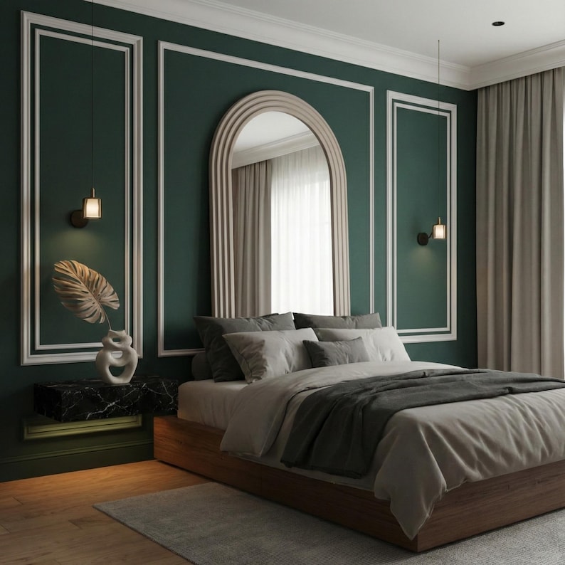 May include: A modern bedroom with a dark green accent wall and white trim. A large arched mirror hangs above the bed, which has gray bedding and a wooden frame. A decorative vase with a leaf sits on a black marble nightstand.