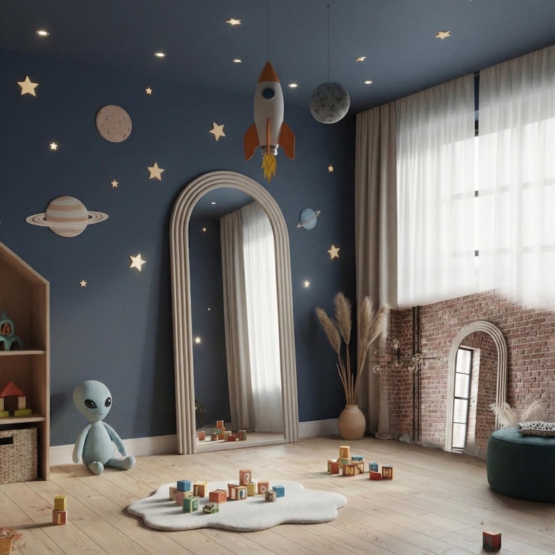 May include: A child's bedroom with a space theme. The room features a blue wall with star and planet decorations, a large arched mirror, and a rocket ship hanging from the ceiling. A plush alien toy sits on the floor near a cloud-shaped rug with wooden blocks.