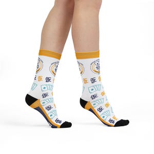Può includere: Calzini bianchi con polsino e tallone gialli, con un design a tema casinò. I calzini mostrano semi di carte da gioco, il numero 10 e il testo "American Casino League". I calzini sono indossati sulle gambe di una persona.