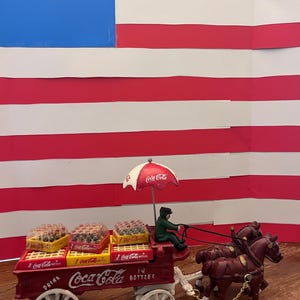 May include: A white ceramic mug with a black handle and the text "But First, Coffee" in a black, bold font. The mug is sitting on a white surface. The mug is approximately 4 inches tall.