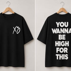 May include: A black short-sleeve t-shirt featuring a white XO logo with a small heart on the front chest. The back of the shirt displays the white text YOU WANNA BE HIGH FOR THIS in a bold, capitalized, sans-serif font. The shirt hangs on a hanger.