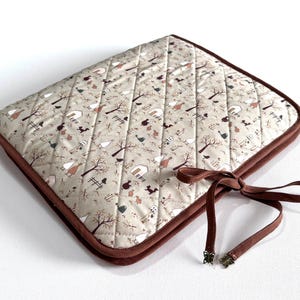 Può includere: Tessuto trapuntato beige con motivo a tema fattoria, con alberi, case e animali. Bordi marrone scuro e fiocco di nastro abbinato. Di forma quadrata.